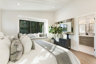Modern bedroom with a large bed, window seat, and bathroom in the background.