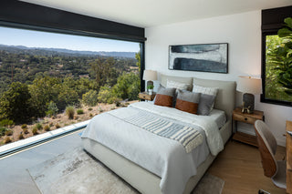 Modern bedroom with large windows offering a scenic view of trees and mountains.
