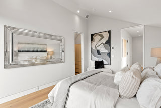 Modern bedroom with a bed, mirror, and abstract art on the wall.