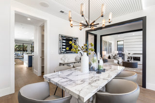 Modern dining room with marble table and chairs, featuring a chandelier and artwork on the wall.