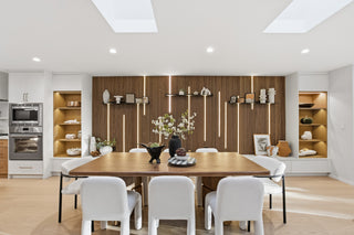 Modern dining room with wooden table and white chairs, featuring a decorative wall with shelves.