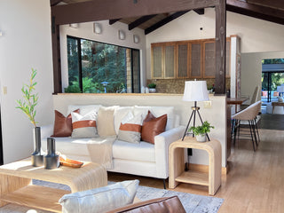 Modern dining room with a wooden table, six chairs, and a large round light fixture. Sunlight streams through large windows, highlighting an cozy, inviting atmosphere.