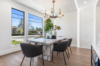 Modern dining room with marble table and black chairs, large windows, and chandelier.