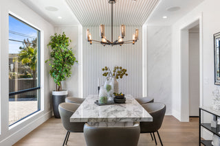 Modern dining room with marble table and gray chairs, large windows, and decorative plants.