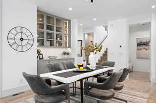 Modern dining rooms with a white table and gray chairs, featuring a clock on the wall.