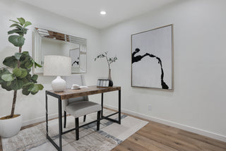Modern home office with a desk, chair, lamp, and artwork on a white wall.
