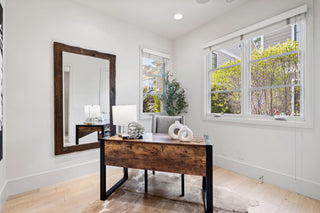 Modern home office with wooden desk, mirror, and large windows.