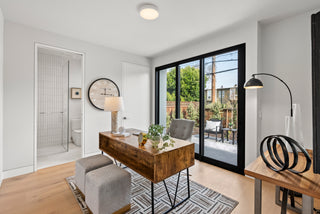 Modern home office with wooden desk, gray chairs, and large windows.