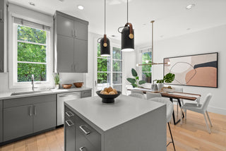 Modern kitchen and dining area with gray cabinets, island with bowl of bread, abstract art, and large windows letting in natural light.