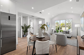 Modern kitchen and dining area with stainless steel refrigerator, wooden table, and white chairs.