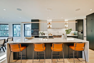 Modern kitchen with white island, orange bar stools, and large windows.