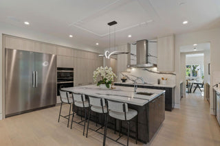 Modern kitchen with large marble-topped island, five bar stools, built-in stainless-steel appliances, and elegant lighting. Bright, spacious, and stylish.