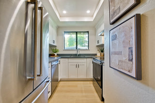 A Modern kitchen with stainless steel refrigerator, black stove, and white cabinets.