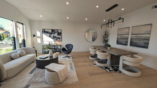 Modern living and dining area with light wood flooring, featuring a gray couch, abstract art, round mirror, and a stylish dining table set for six. Bright and airy ambiance.