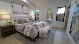 Modern living and dining area with light wood flooring, featuring a gray couch, abstract art, round mirror, and a stylish dining table set for three. 