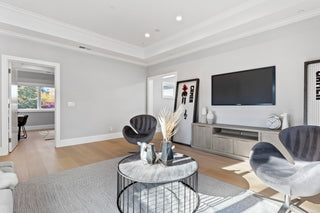 Modern living room featuring light wood floors, gray walls, a circular black wire coffee table, two dark velvet swivel chairs, and a wall-mounted television above a media console.