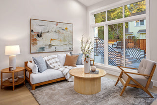 Modern living room with a sofa, coffee table, and armchair near large windows and wall printing