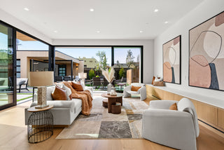 Modern living room with white furniture, abstract art, and large windows.