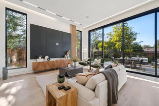 Modern living room with large windows, beige sofa, and wooden coffee table glass wall side view nature