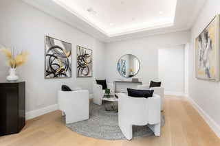 Modern living room with light bouclé seating, abstract art, and a view through a doorway to a grand staircase and black baby grand piano.