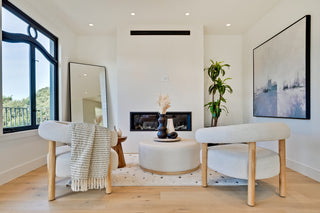 Modern living room with white chairs, a round ottoman, and a fireplace.