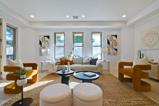 Modern living room with orange chairs, white ottomans, and a coffee table.