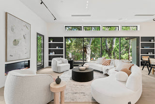 Modern living room with white furniture, large windows with glass, and a view of trees and nature