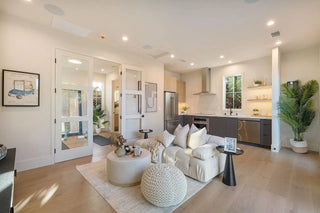 Modern living room with white furniture, plants, and a kitchen in the background. cute night