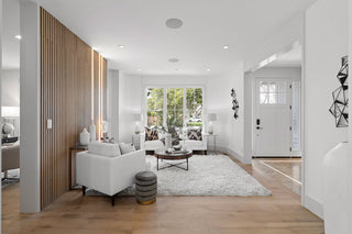 Modern living room with white furniture, wooden floor, and large windows.