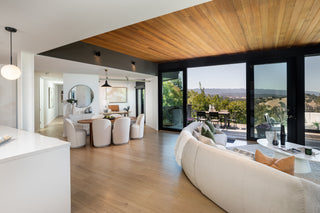 Modern living room with large windows, wooden floor, and outdoor view.