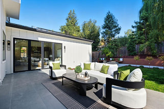 Modern outdoor patio with white furniture, greenery, and a clear blue sky.