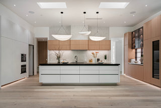  Natural light highlights clean lines and a spacious layout. Modern kitchen with sleek wood and white cabinetry, black countertops, and elegant decor.