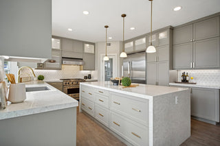 Nice_Kitchen_featuring_light_gray_shaker_cabinets_a_large_white_quartz_island_with_gold_hardware_stainless_steel_appliances_and_three_brass_pendant_lights_above_the_island.