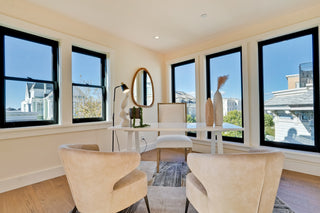 Modern living room with large windows, beige chairs, and a white table.