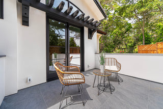 Outdoor patio area with wicker chairs and a small table on a gray deck with full nature of tree with sun