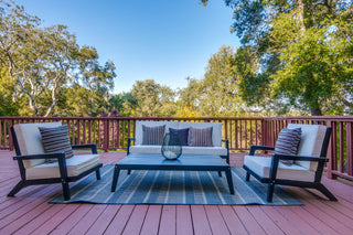 Outdoor patio set with chairs and a table on a wooden deck surrounded by trees.