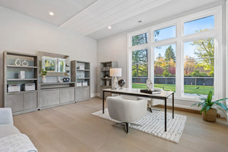 Modern home office with large windows, desk, and bookshelves.