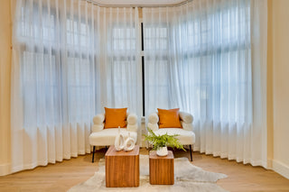 Modern living room with white chairs, orange cushions, and wooden coffee tables in front of large windows.