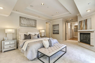 Spacious living room with large windows and wood frames, white walls, and hardwood floors. Cozy beige sofas surround a rustic table. Airy and bright ambiance.