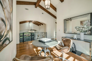 Spacious living room with large windows and wooden frames overlooking a lush garden. Cozy beige sofa with patterned cushions, a rustic wooden coffee table, and modern kitchen in background. Bright and inviting atmosphere.