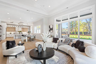 Modern living room with white furniture, large windows, and a view of a garden.