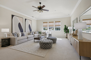 Spacious living room with neutral tones, featuring a large beige sectional sofa, abstract wall art, tufted ottomans, and a ceiling fan. Bright and serene.