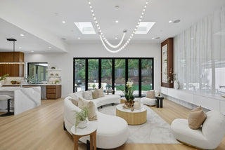 Modern living room with white furniture, wooden floors, and large windows.