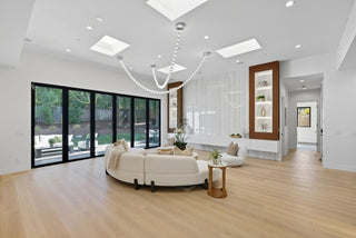 Modern living room with white furniture, large windows, and a chandelier.