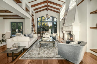 Spacious, modern living room with white sofas, colorful cushions, wooden coffee table, and abstract art. Natural light from skylights and large windows.