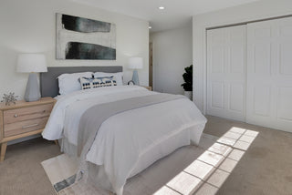 Stunning bedroom with two single beds featuring white and orange bedding, black metal frames, and matching artwork. Soft lighting and neutral tones create a calm, inviting atmosphere. Pink poufs and a patterned rug complete the decor.