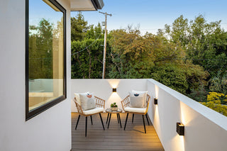 Stylish outdoor patio with two chairs, cushions, and a small table on a wooden deck. Surrounded by trees, creating a peaceful evening ambiance.