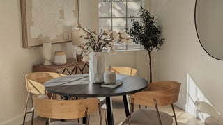 Dining room with a round table and chairs, featuring a vase with flowers and decorative items.