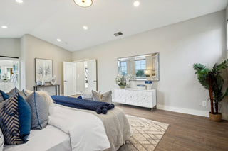 bedroom_featuring_a_white_and_blue_bedding_set_dark_wood_floors_and_a_white_geometric_dresser_topped_with_a_large_mirrored